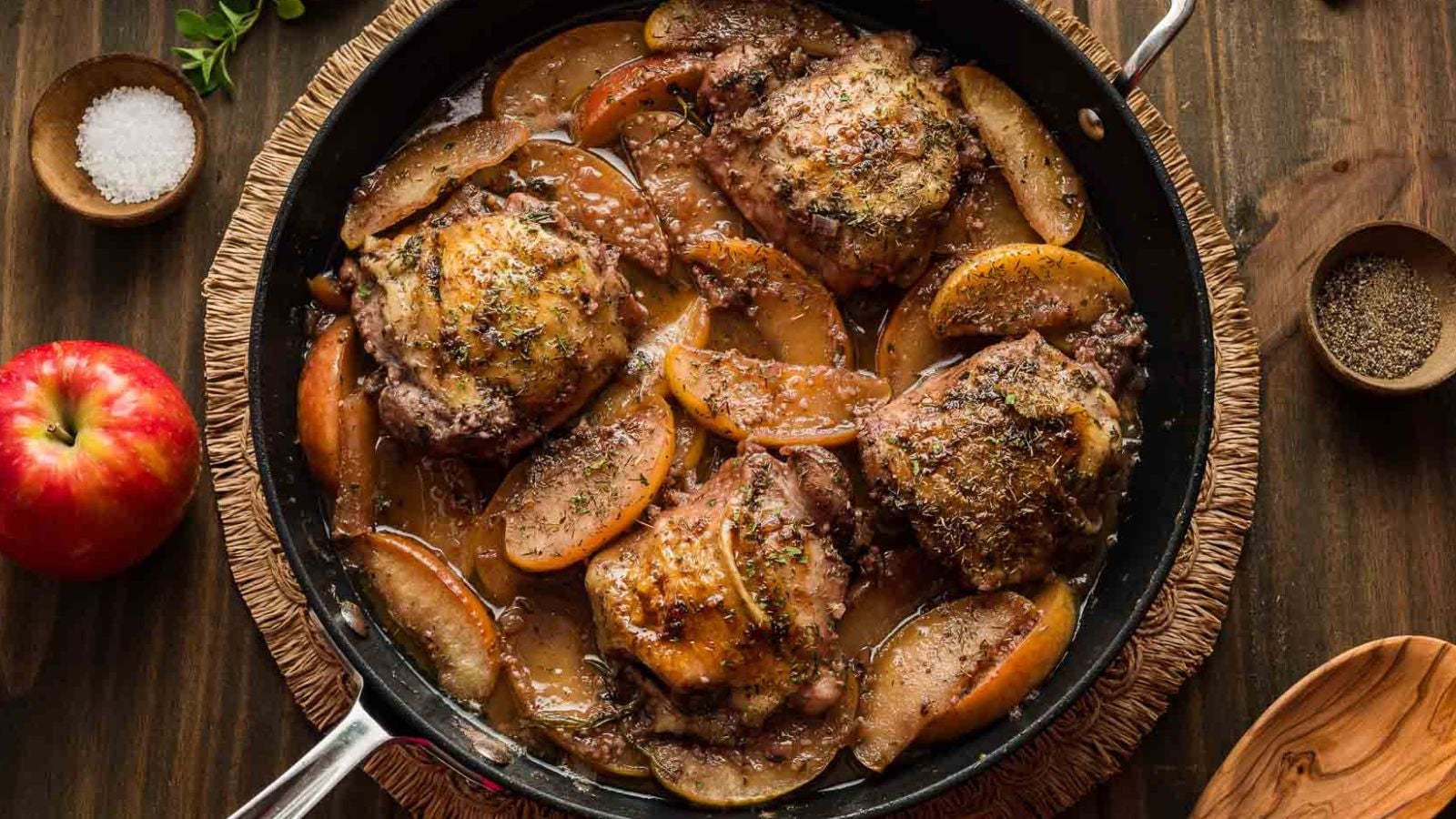 Chicken thighs simmered in apple cider with herbs and golden browned skin in a skillet.