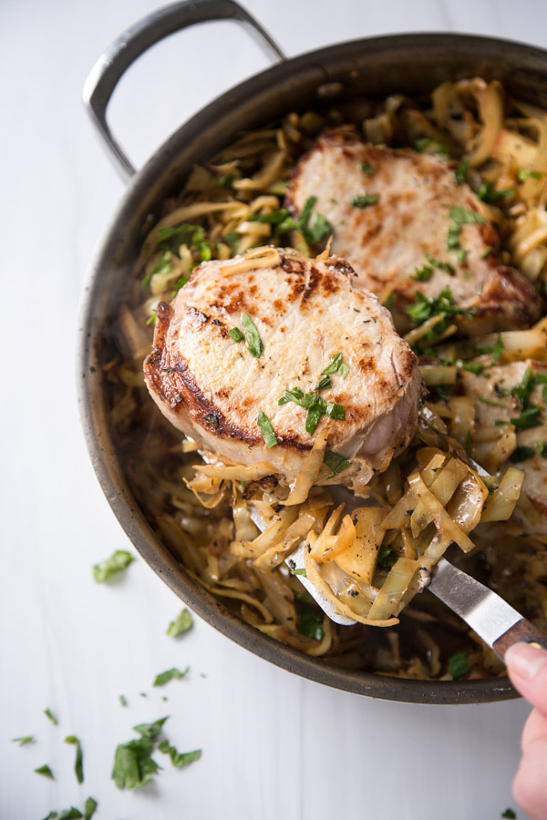 pan fried boneless pork loin chops in a skillet with cabbage, apples and spatula