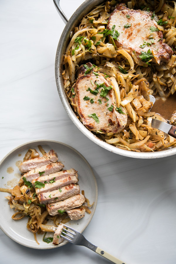 seared boneless pork loin chops in a skillet with cabbage, apples and spatula next to plate