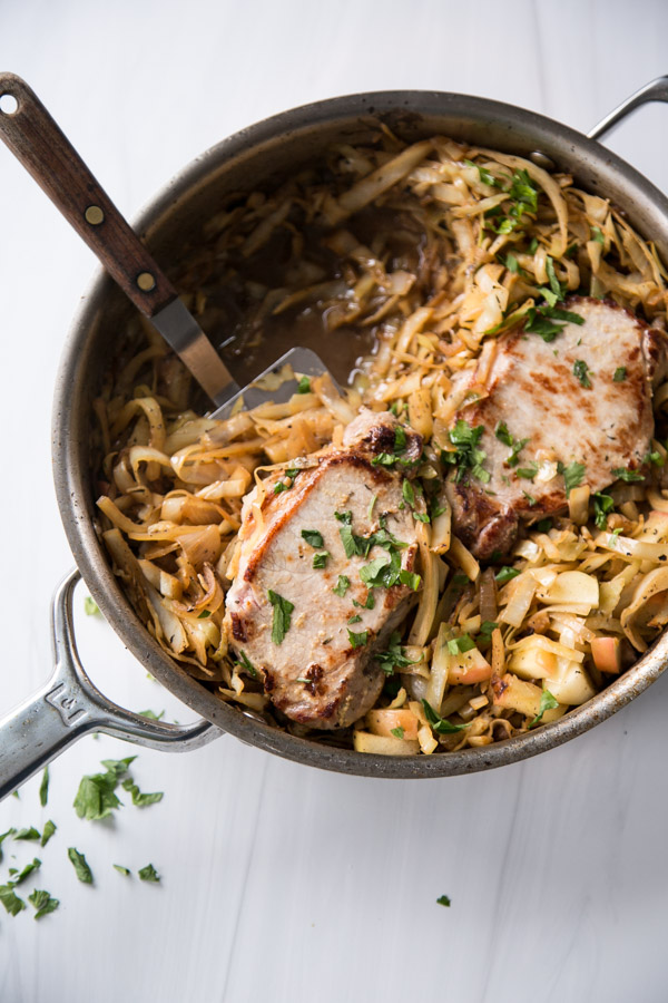 pan fried boneless pork loin chops in a skillet with cabbage, apples and spatula