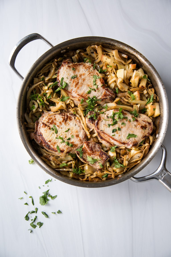 seared boneless pork loin chops in a skillet with cabbage and apples and herbs