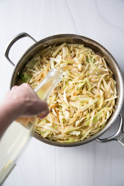 cabbage with hand pouring white wine over skillet