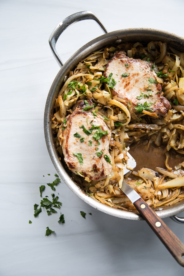 seared boneless pork loin chops in a skillet with cabbage, apples and spatula