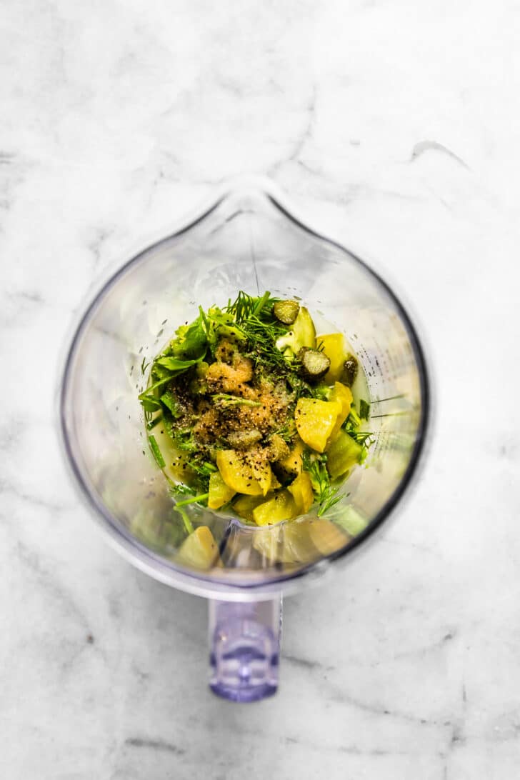 Blender filled with chopped pickles, fresh herbs, avocado, and seasonings before being mixed into dressing.