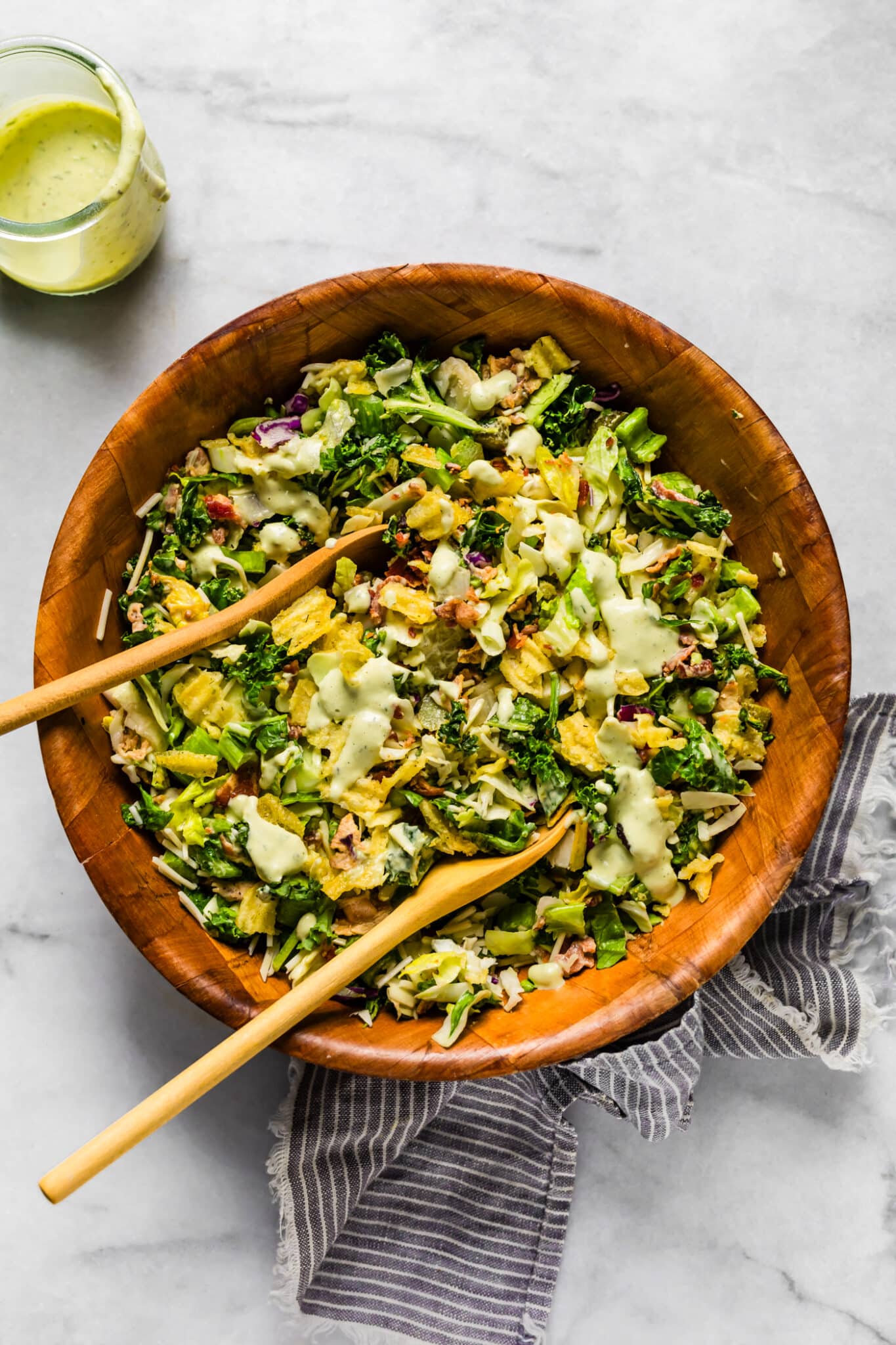 Large bowl of chopped salad tossed with creamy dressing, with extra dressing served on the side.