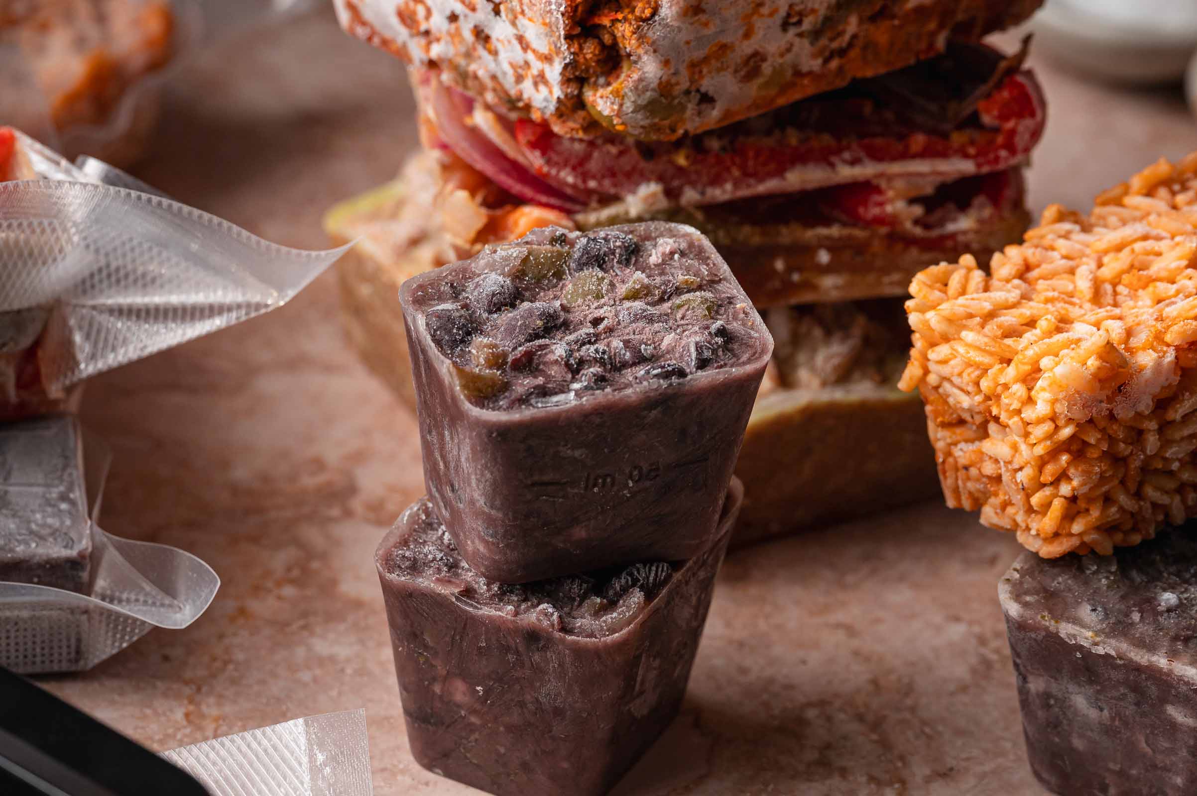 Frozen food items, including two cubes of cuban black beans, a block of spanish rice, and vacuum-sealed packages, are arranged on a countertop.