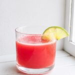 Glass of chilled watermelon drink garnished with a fresh lime wedge.
