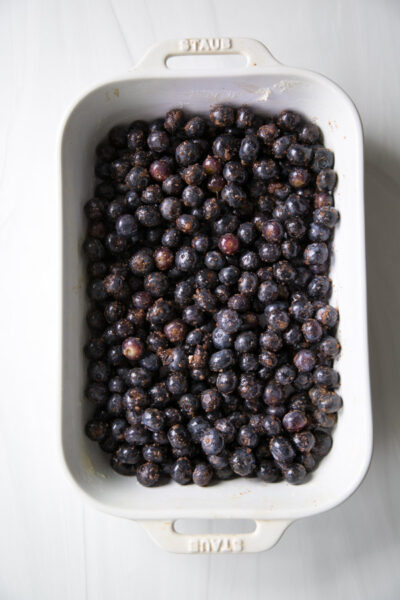 A white rectangular baking dish filled with fresh, sugared black grapes sits on a light marble surface, perfect for a gluten-free treat or as inspiration for your next almond flour or blueberry cobbler recipe.