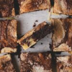 A gluten free cookie brownie cut into 9 squares. The middle square is standing up, showing the fudgy brownie and melted chocolate chips in the baked cookie batter.
