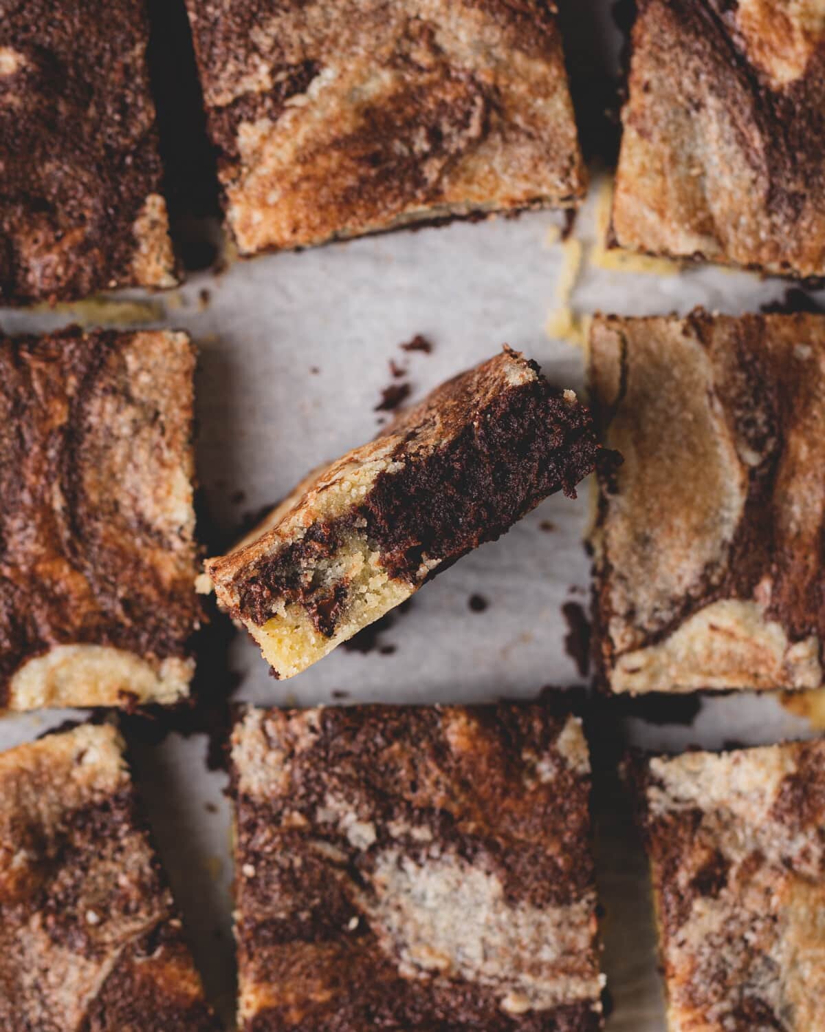 A gluten free cookie brownie cut into 9 squares. The middle square is standing up, showing the fudgy brownie and melted chocolate chips in the baked cookie batter.