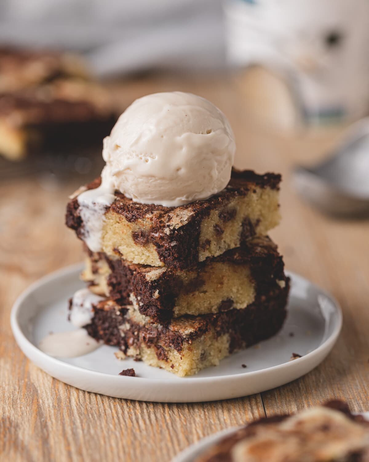 Three gluten free brookie squares stacked on a white plate with a scoop of vanilla ice cream on top. The ice cream is melting down the left side.