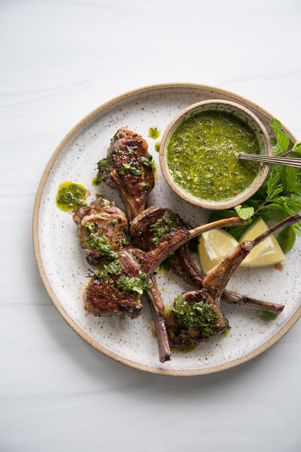 marinated lamb chops on a platter with mint sauce in a bowl