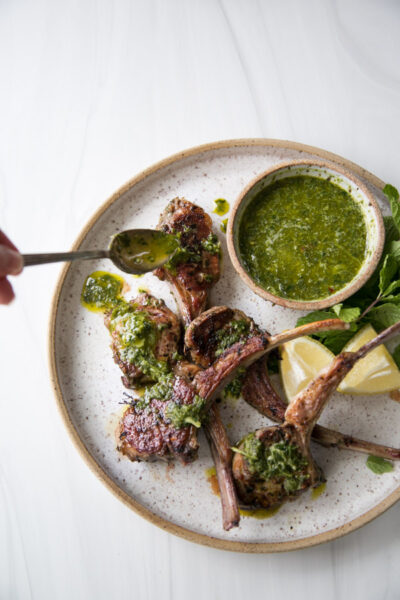 hand drizzling baked lamb rib chops with mint sauce on a platter