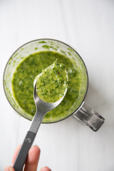 spoon holding mint marinade for lamb chops over a food processor