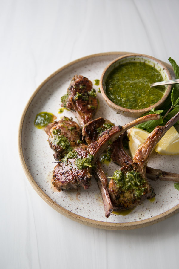 marinated lamb rib chops on a platter with bowl of mint sauce and lemon wedges