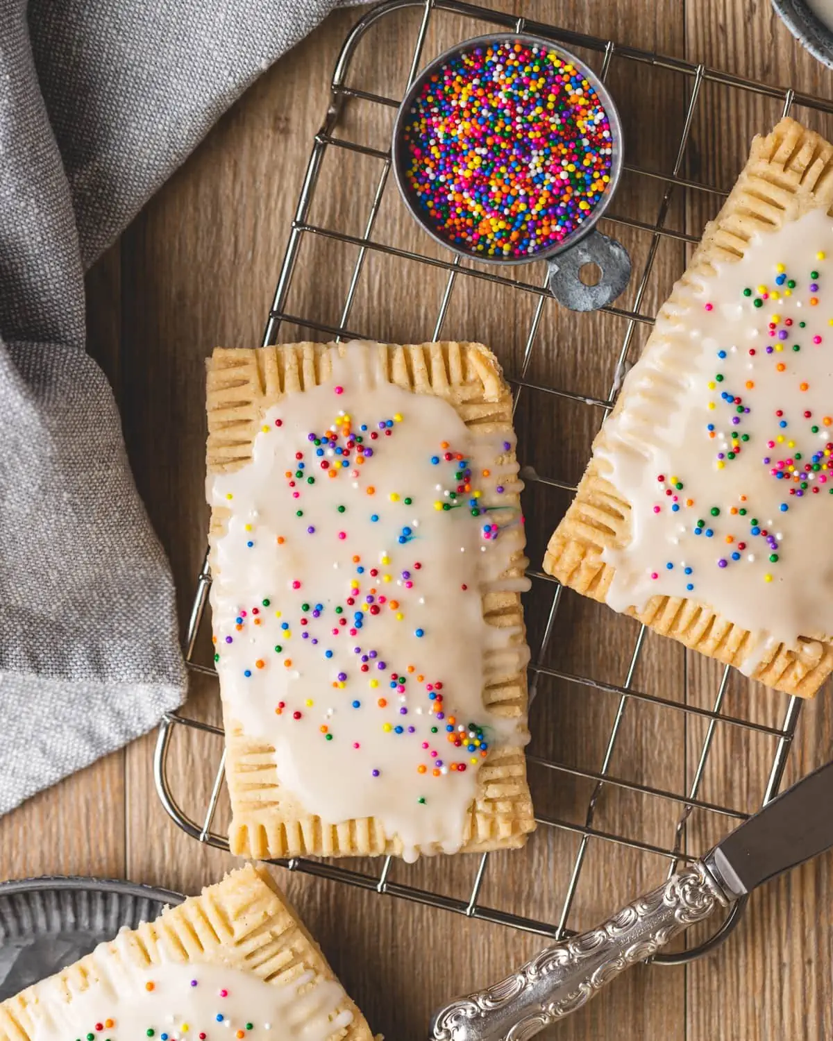 Gluten free pop tarts with white icing and sprinkles on a wire cooling rack.
