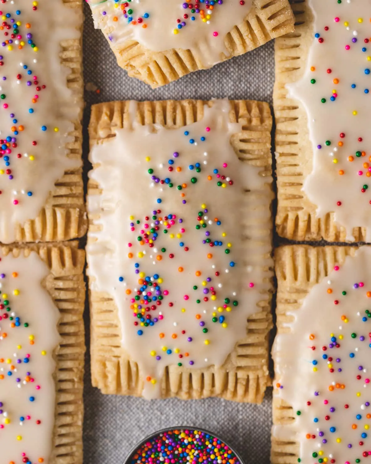 Six pop tarts laid side-by-side with a small bowl of sprinkles at the bottom middle.