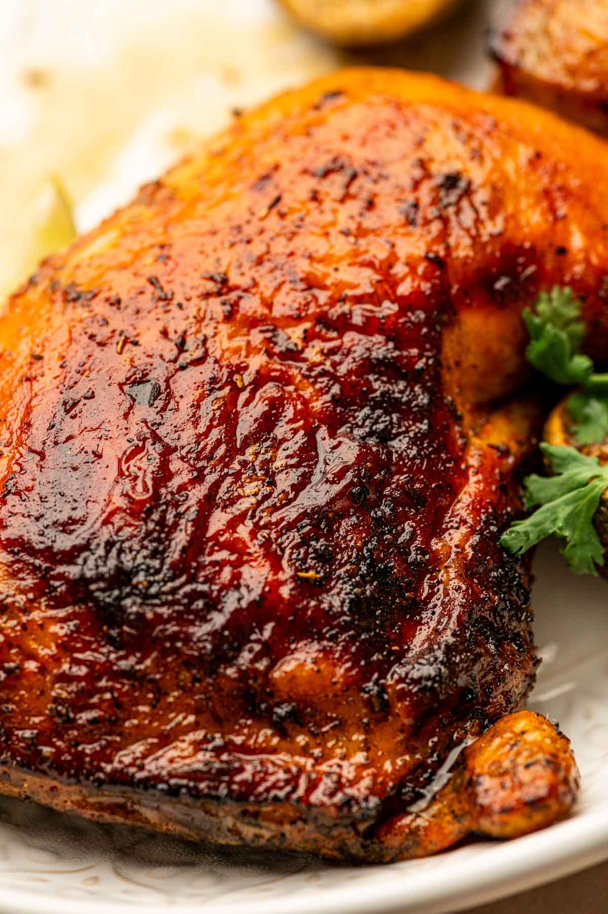 Close-up of a cooked, seasoned chicken thigh with a glazed, crispy skin, garnished with fresh parsley on a white plate.