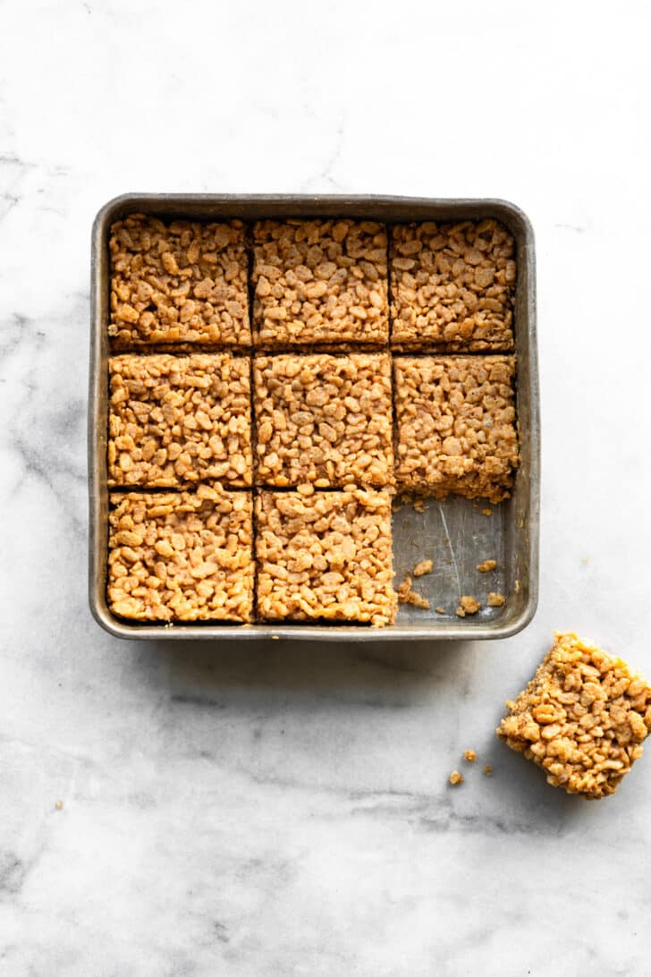 Homemade rice crispy bars pressed into a square baking cut into squares with one piece sitting out of the pan