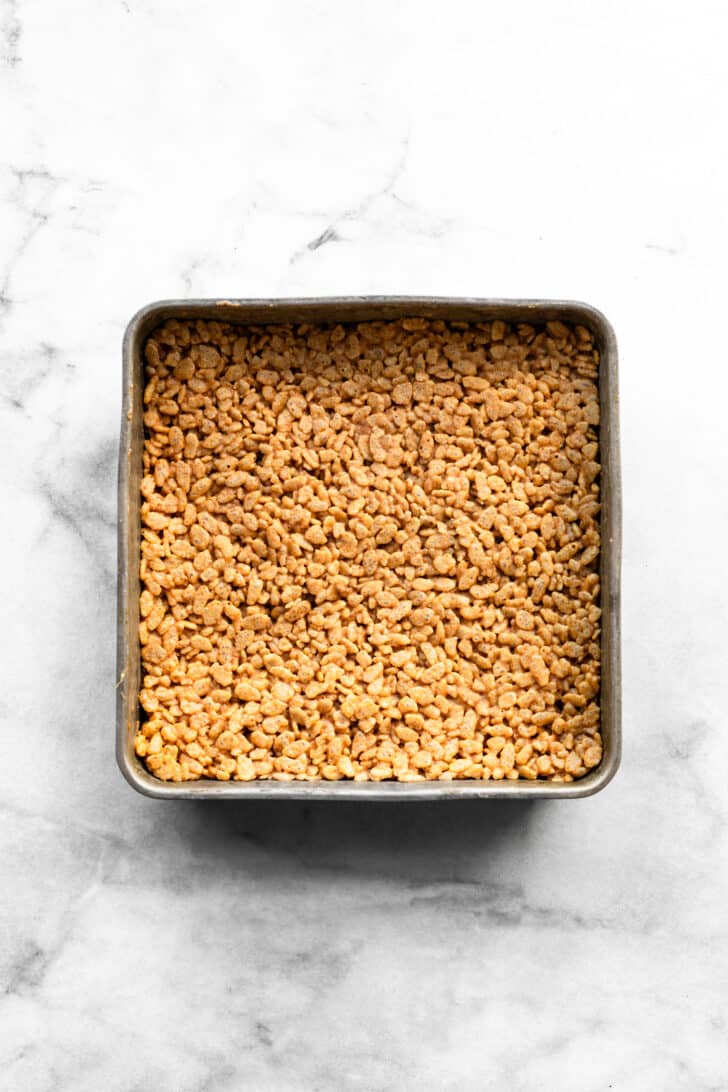 Homemade rice crispy bars pressed into a square baking pan before slicing.
