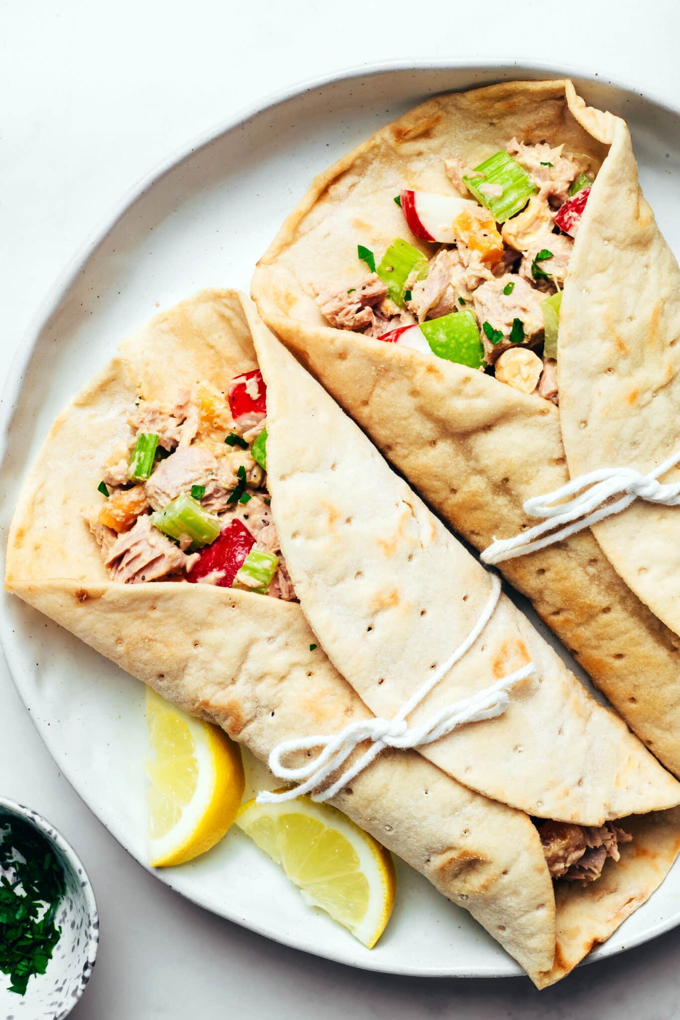 Tuna salad wrapped in soft flatbread wraps with lemon wedges on the side.