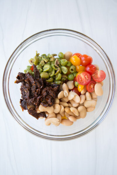 ingredients for gluten-free pasta salad in a bowl - tomatoes olives sundried tomatoes beans