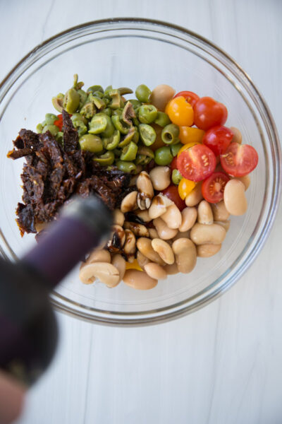 balsamic pouring over tomatoes for gluten-free pasta salad in a bowl