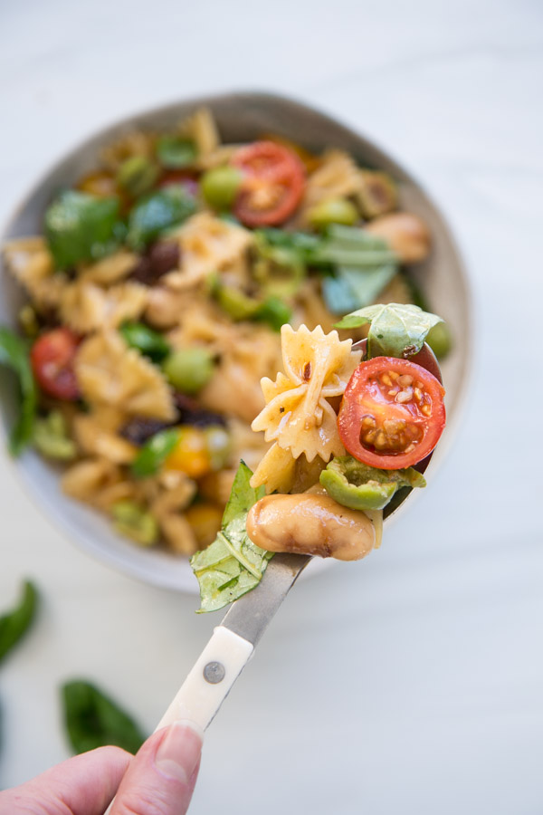 spoon holding dairy-free gluten-free italian pasta salad including tomato farfalle olive basil and white bean