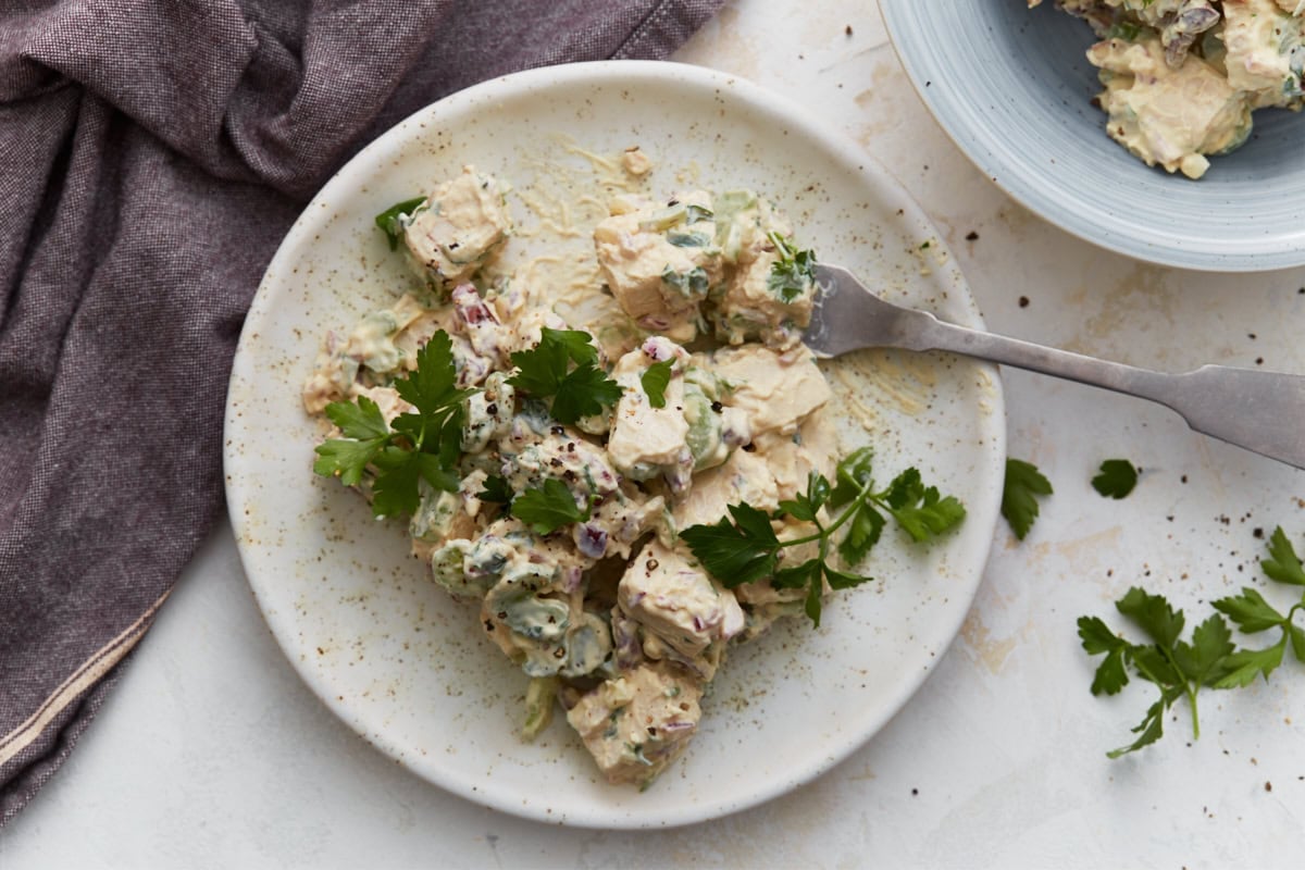 Close-up of keto chicken salad on a white plate with a fork resting beside it, garnished with fresh parsley.