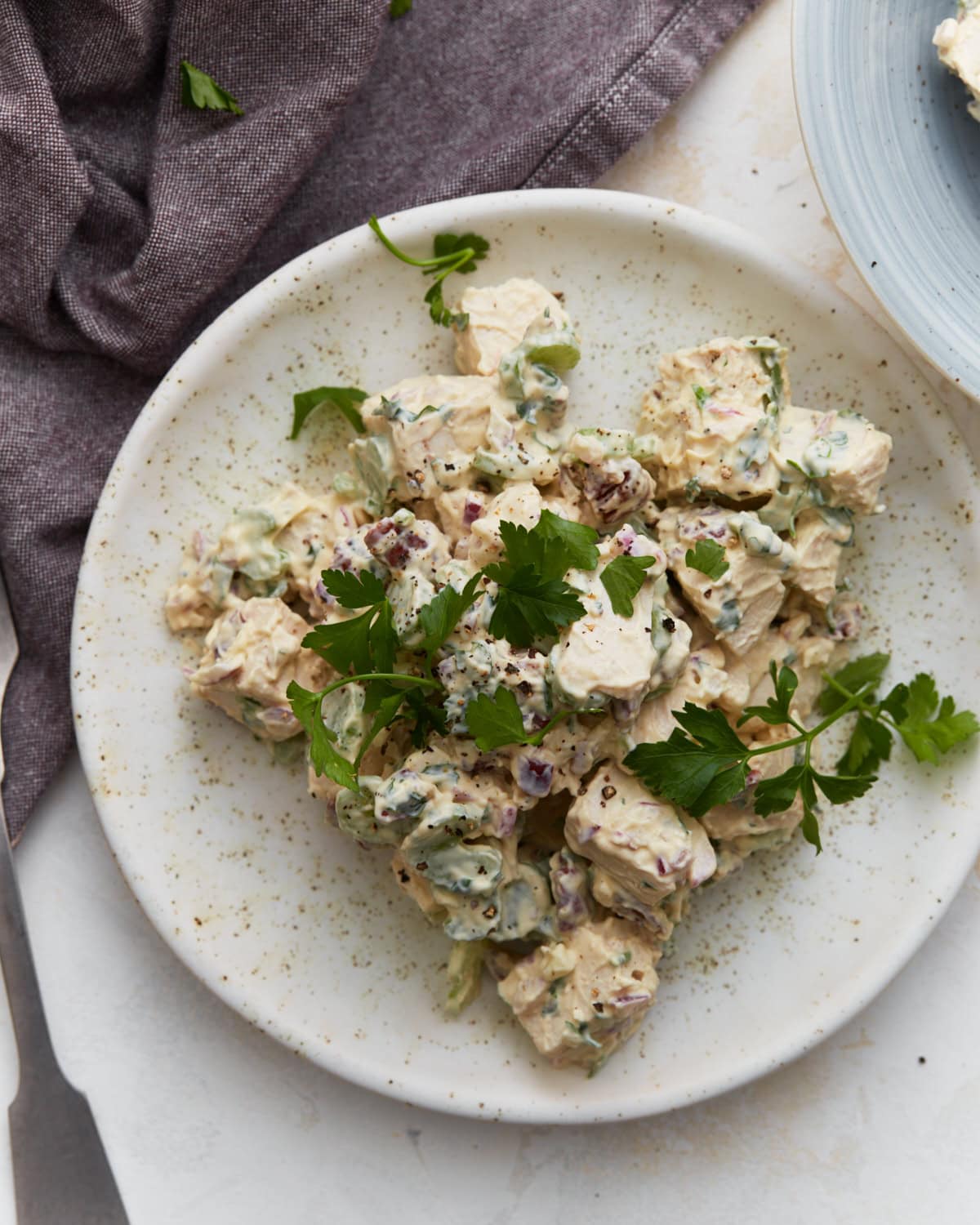 Keto chicken salad on a white plate garnished with fresh parsley, with a purple napkin and second plate in the background.