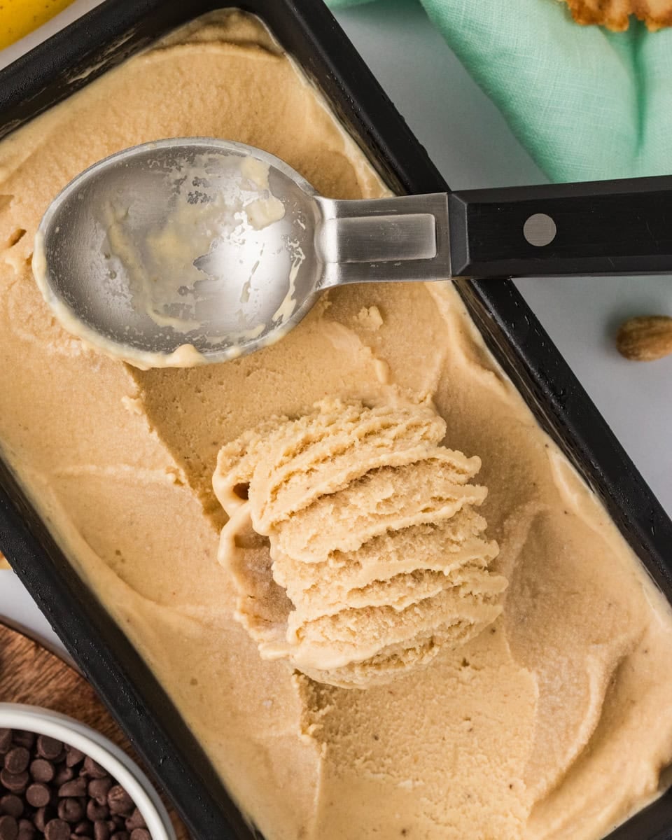 Overhead view of banana peanut butter nice cream being scooped from a black loaf pan with an ice cream scoop