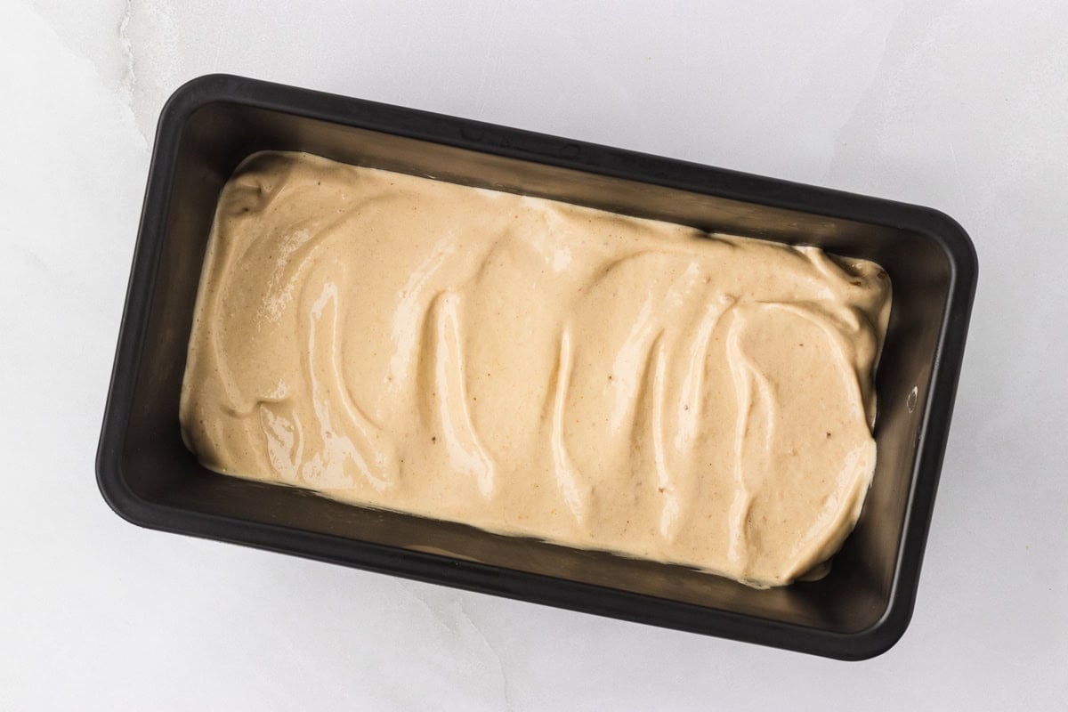 Overhead view of banana peanut butter nice cream mixture transferred and smoothed into a black loaf pan ready to freeze