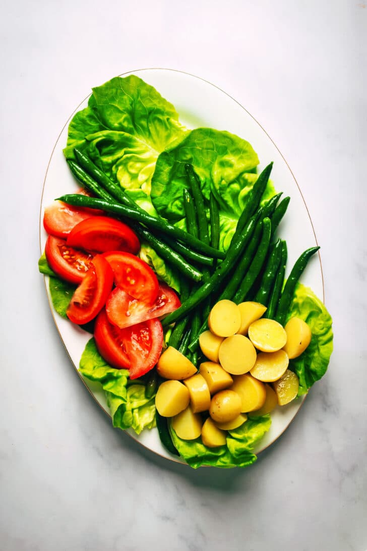 Salad greens, sliced tomatoes, new potatoes, and green beans on an oval platter.