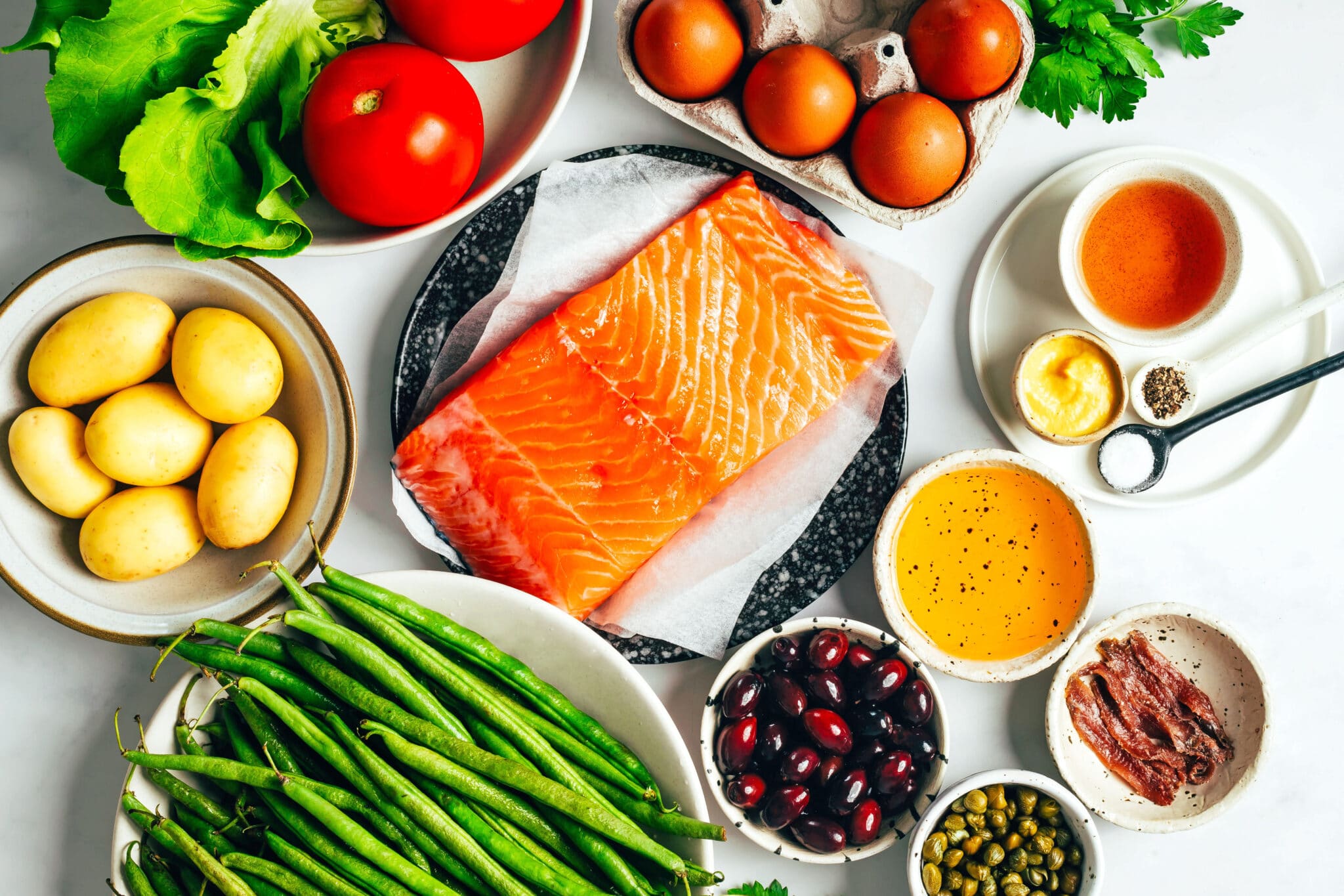 Ingredients for a salmon nicoise salad sitting on a white marble surface.