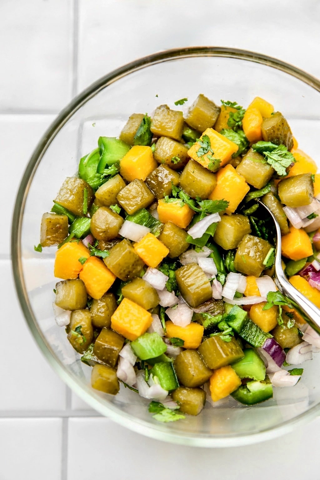 Glass bowl of diced pickles and mango mixed with herbs, onion, and green pepper.