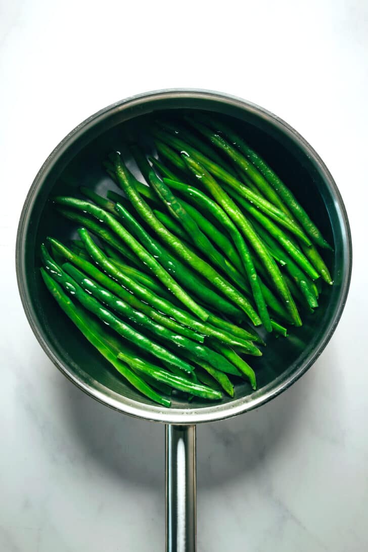 A sauce pan with green beans in water.