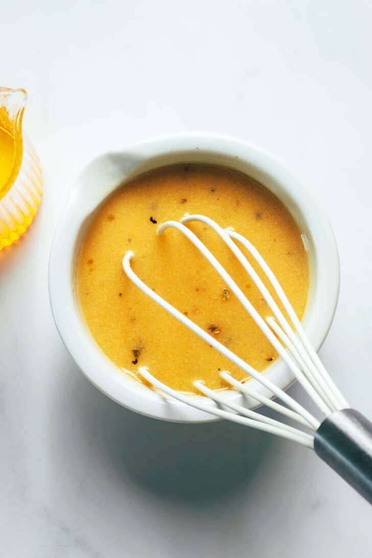 A white whisk in a small bowl of Dijon vinaigrette