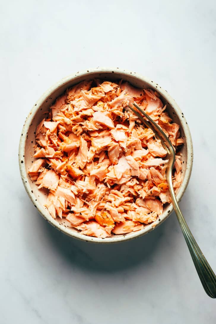 A fork in a bowl of cooked and flaked salmon.