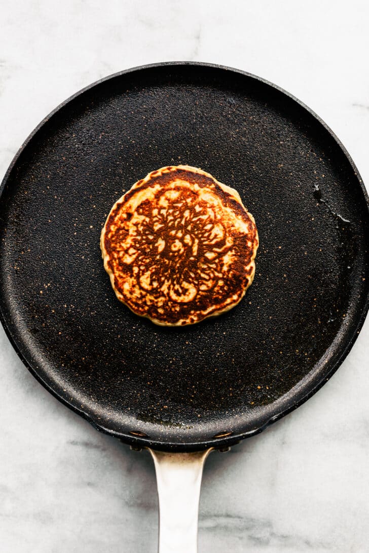 4. Single gluten-free pancake cooking in a skillet, showing a golden-brown surface after flipping.