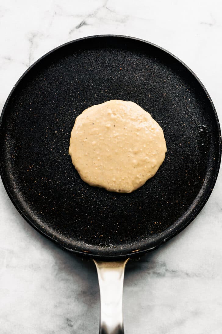 5. Gluten-free pancake batter poured into a hot skillet, spreading into a round shape.