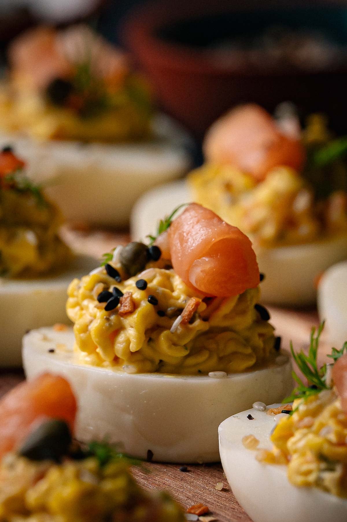 Close-up of deviled eggs topped with a swirl of smoked salmon, capers, sesame seeds, and fresh dill.
