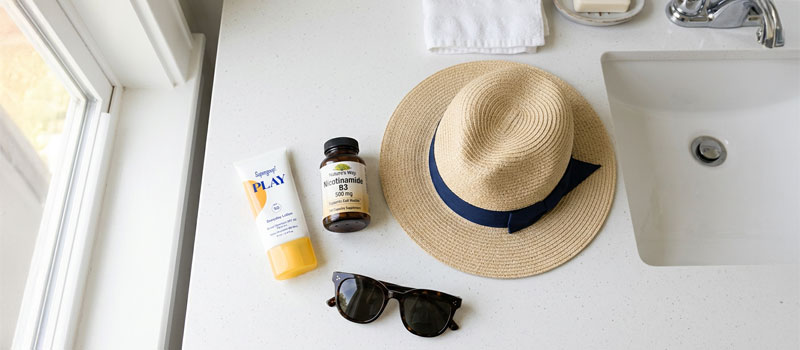 Sunscreen, supplements, hat, and sunglasses arranged as a complete UV skin protection kit