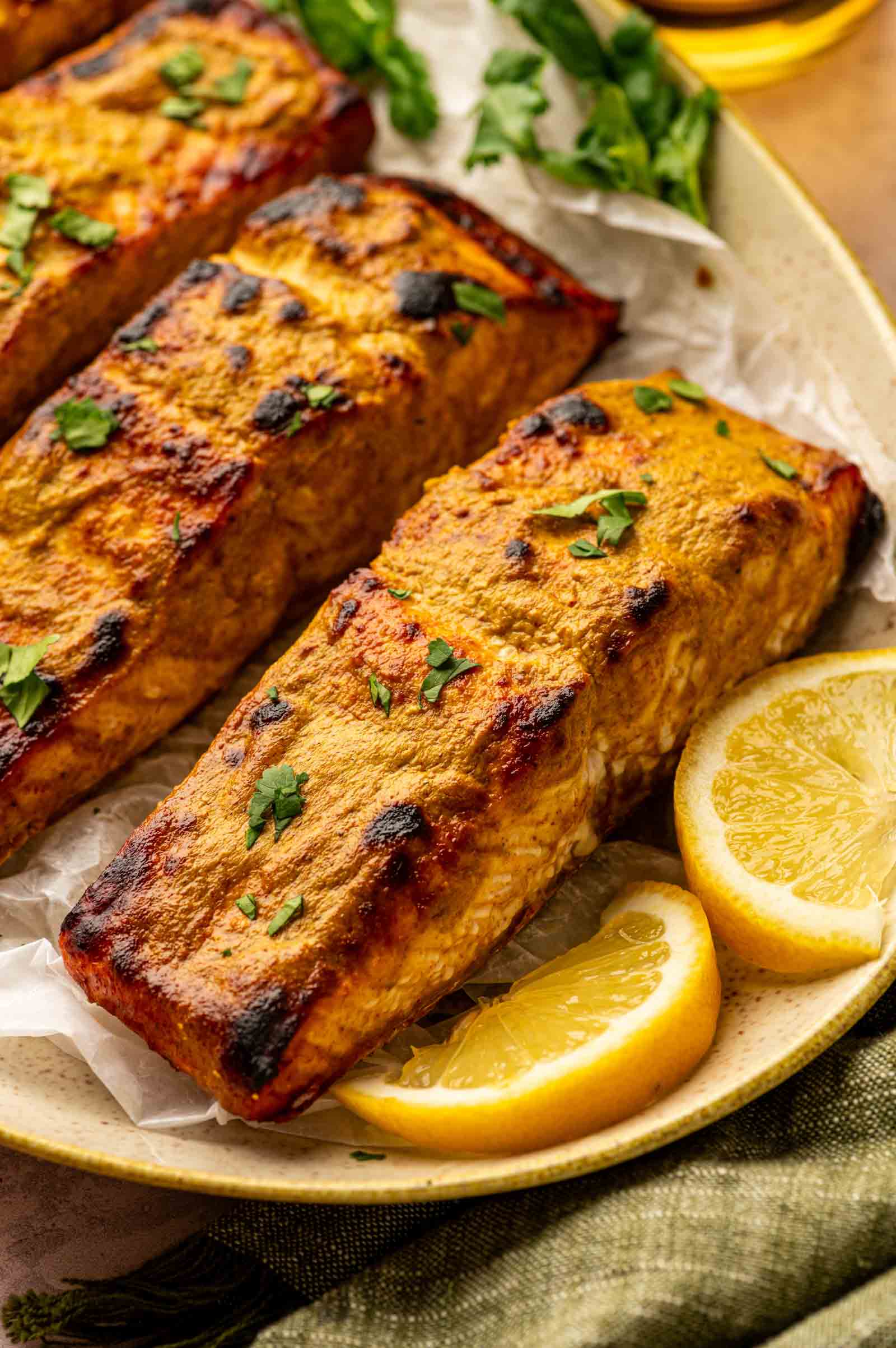 Three pieces of baked salmon fillet garnished with chopped herbs, served on a plate with lemon wedges and fresh greens.
