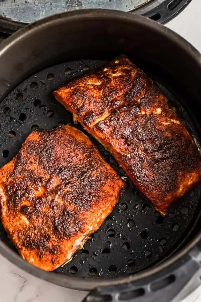 Two blackened salmon fillets in an air fryer basket. 