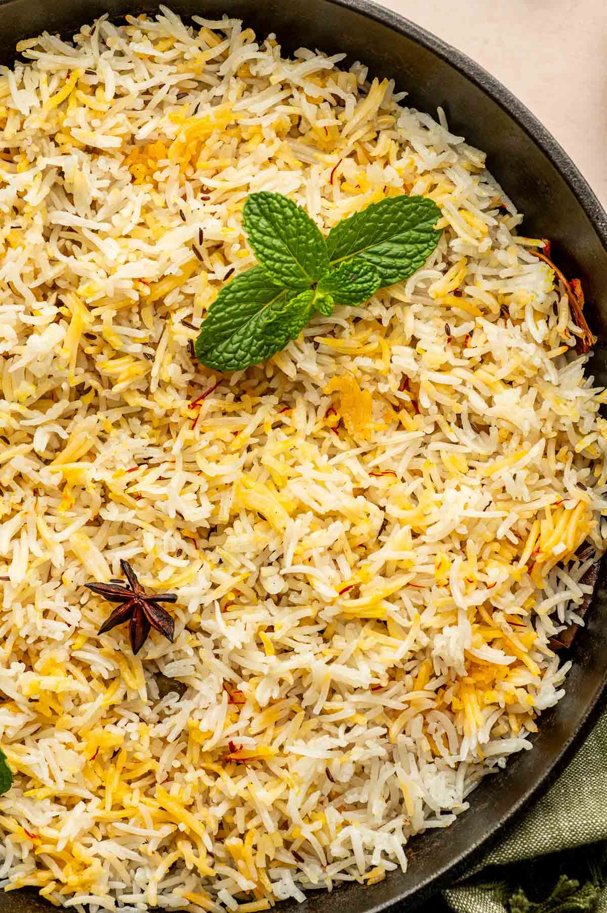 A plate of cooked basmati rice garnished with a sprig of mint and a star anise.