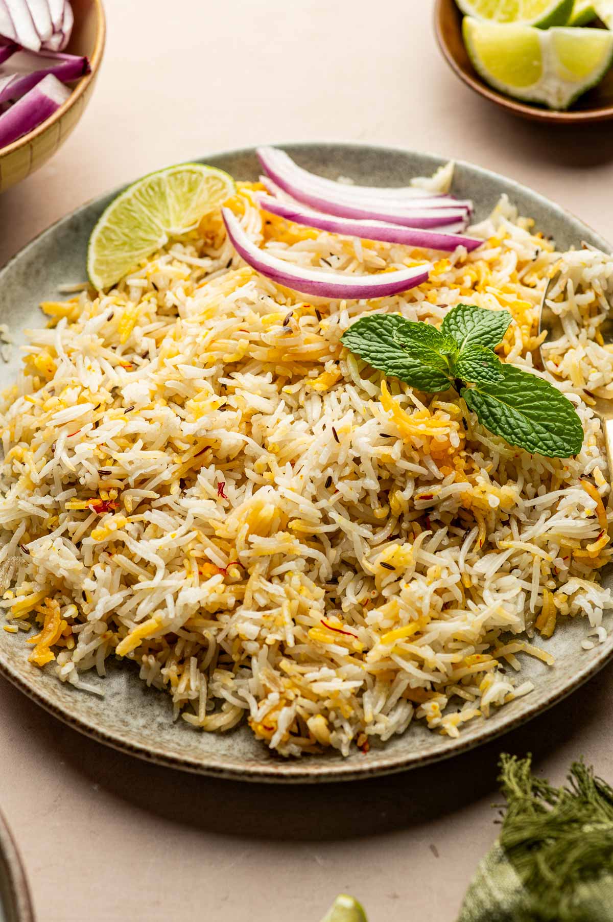 A plate of cooked biryani rice garnished with a lime wedge, sliced red onions, and fresh mint leaves.