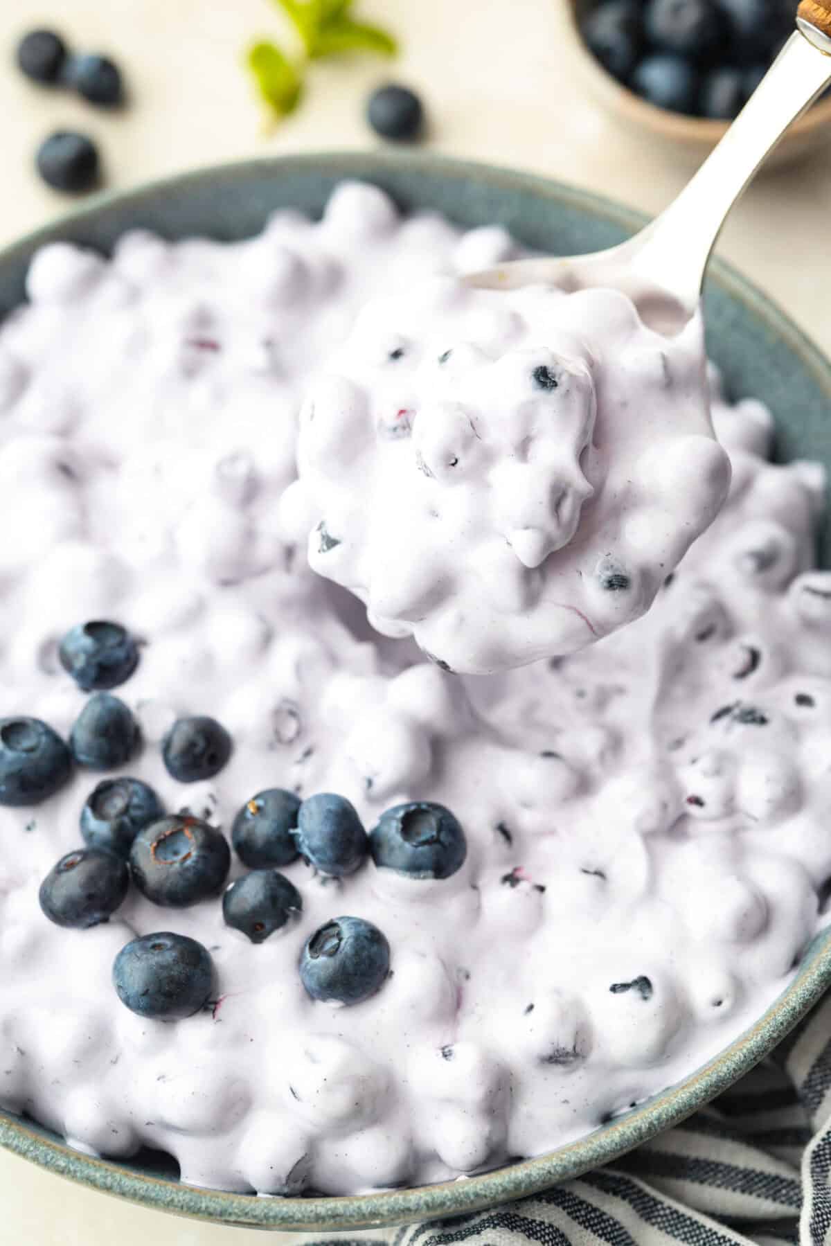 Close up of  someone lifting up a serving sized spoonful of blueberry fluff. 