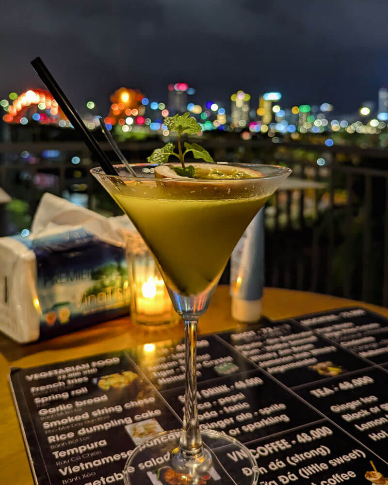Cocktail in a martini glass served at a rooftop bar with the city of Da Nang in the backgrounf