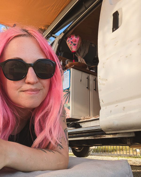 Girl lying next to open campervan, enjoying the sun