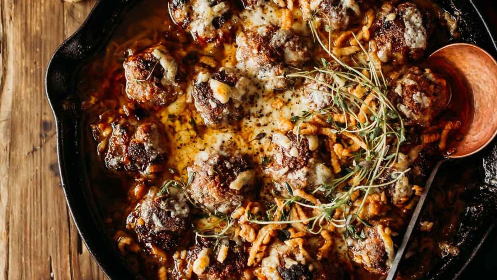 French onion meatballs covered in melted cheese and caramelized onions in a deep skillet.